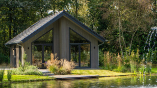 Ecovilla Waterzicht Comfort lodge by a pond, set in a natural, green landscape with large windows and trees.