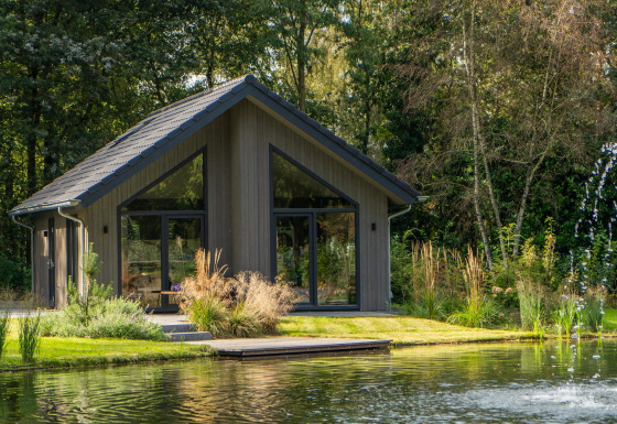 Ecovilla Waterzicht Comfort lodge by a pond, set in a natural, green landscape with large windows and trees.