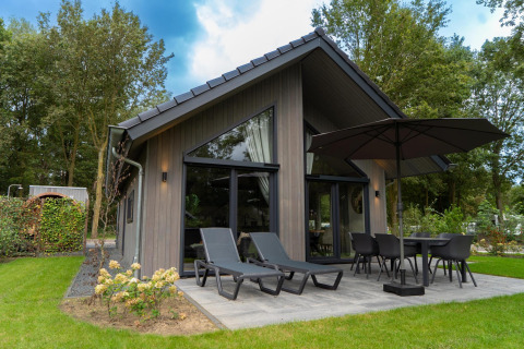 Vista exterior de Ecovilla Waterzicht Comfort Sauna & Buitendouche con terraza, tumbonas y sombrilla.