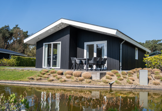 Moderne sort Villa Waterzicht Comfort-lodge med udendørs spisebord, omgivet af natur og dam