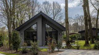 Modern lodge named Ecovilla Boszicht Comfort, surrounded by trees and greenery in a forest setting.