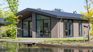 Moderne lodge ved søen, Villa Waterzicht Luxe 4, med store vinduer og grønne omgivelser, solrig dag