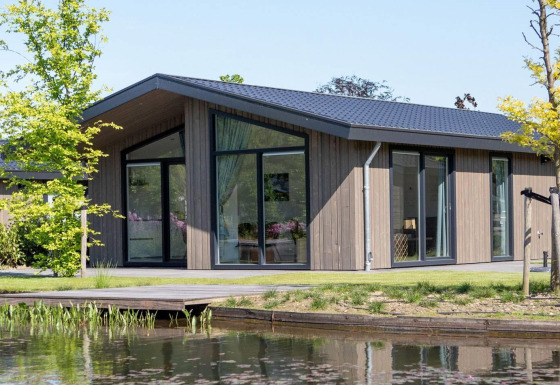 Moderne Villa Waterzicht Luxe 4 Lodge am Wasser mit großen Fenstern und Garten an einem sonnigen Tag
