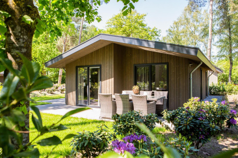Villa Bosrand Comfort lodge with wooden exterior, patio seating area, surrounded by flowers and greenery.