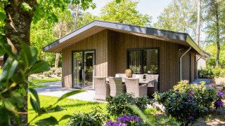 Lodge Villa Bosrand Comfort con rivestimento in legno, tavolo da esterno e fiori in un giardino verde.