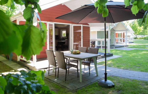Zona de comedor exterior con sombrilla en Lodge Deluxe Plus, rodeada de vegetación y otras cabañas cercanas.