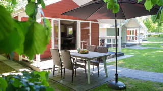 Zona de comedor exterior con sombrilla en Lodge Deluxe Plus, rodeada de vegetación y otras cabañas cercanas.