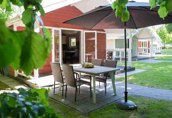 Zona de comedor exterior con sombrilla en Lodge Deluxe Plus, rodeada de vegetación y otras cabañas cercanas.