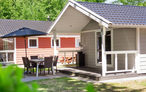 Vista exterior de Lodge Deluxe con terraza, muebles de jardín y sombrilla, rodeada de naturaleza verde.