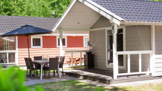 Vista exterior de Lodge Deluxe con terraza, muebles de jardín y sombrilla, rodeada de naturaleza verde.