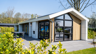 Moderne hytte i træ og glas med terrasse og have, set fra siden, beliggende ved Wood Lodge Waterzicht.