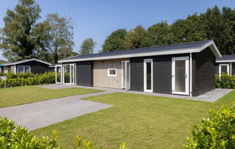 En moderne Wood Lodge med sort facade, hvide rammer og velplejet græsplæne foran, omgivet af træer.