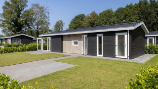 En moderne Wood Lodge med sort facade, hvide rammer og velplejet græsplæne foran, omgivet af træer.
