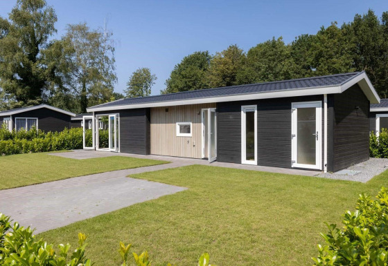 Moderna Wood Lodge con rivestimento scuro, dettagli bianchi e prato curato, circondata da alberi verdi.