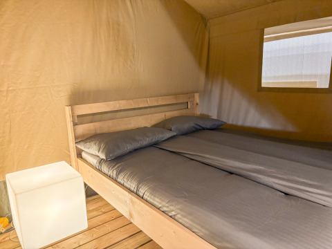 Indvendigt billede af en safariteltsoveplads med dobbeltseng, gråt sengetøj og blødt lys på Camping La Plage.