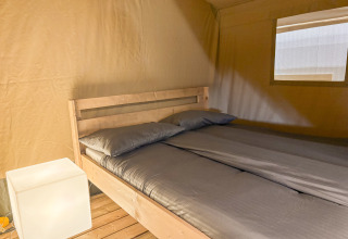 Indvendigt billede af en safariteltsoveplads med dobbeltseng, gråt sengetøj og blødt lys på Camping La Plage.