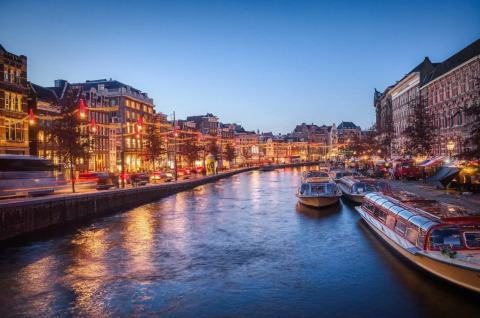 Vista al atardecer de un canal con barcos iluminados y edificios históricos cerca de Uitgeest, Holanda Septentrional.