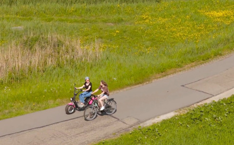 Two people ride bicycles along a paved path surrounded by green grass at Marina Uitgeest, Netherlands.