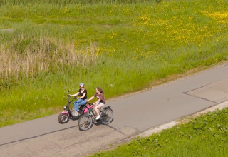 Zwei Personen fahren auf Fahrrädern auf einem Weg durch grüne Wiesen bei Marina Uitgeest, Nordholland.