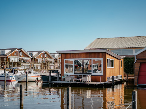 Flydende feriehytte ved Marina Uitgeest med både og moderne hytter i baggrunden, Nordholland, Holland.
