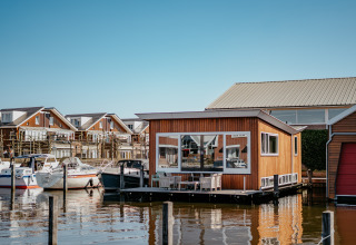 Flydende feriehytte ved Marina Uitgeest med både og moderne hytter i baggrunden, Nordholland, Holland.