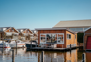 Schwimmendes Ferienhaus im Marina Uitgeest, mit Booten und modernen Häusern im Hintergrund, Nordholland.