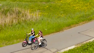 Twee mensen fietsen langs een pad met gras en bloemen bij Marina 'Uitgeest', Noord-Holland, Nederland.