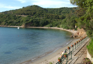 Vista sulla spiaggia e le colline verdi al Campeggio Rosselba le Palme in Toscana, Italia, con mare limpido.