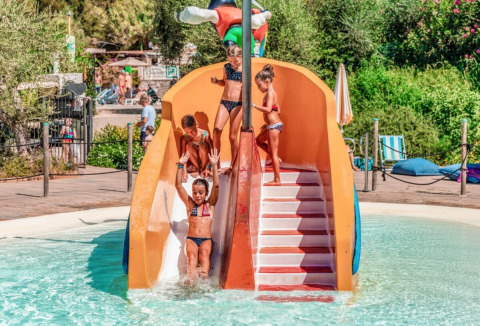 Bambini giocano su uno scivolo d'acqua nella piscina del campeggio Rosselba le Palme in Toscana, Italia.