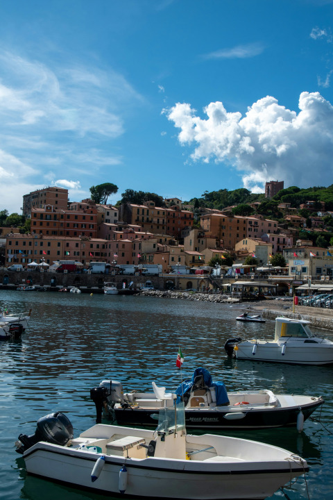 View of Rosselba le Palme campsite harbor in Tuscany, Italy, featuring boats and colorful hillside houses.