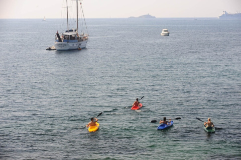 Four people kayaking in the sea near boats around Portoferraio, Tuscany, Italy, on a sunny, calm day.