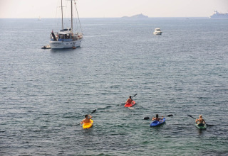 Quattro persone fanno kayak vicino a barche nel mare di Portoferraio, Toscana, Italia, in una giornata soleggiata.