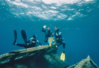 Three snorkelers explore underwater near Portoferraio, Tuscany, Italy, waving at the camera in clear blue water.