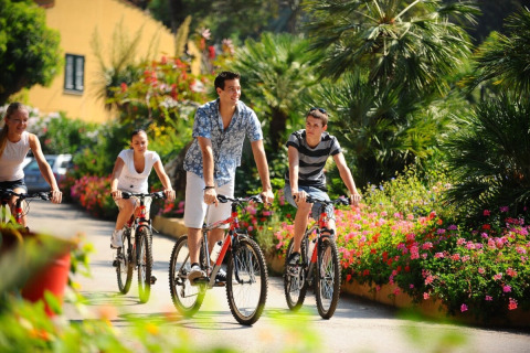 Quattro persone pedalano lungo un sentiero fiorito al campeggio Rosselba le Palme in Toscana, Italia.
