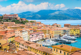 View of Portoferraio, Tuscany, Italy, featuring colorful buildings, a marina with yachts, and hills beyond.