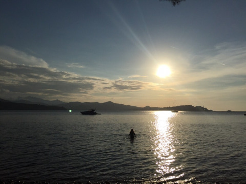 Sunset over the sea with boats and a person swimming at Campsite Rosselba le Palme in Tuscany, Italy.