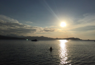Sunset over the sea with boats and a person swimming at Campsite Rosselba le Palme in Tuscany, Italy.