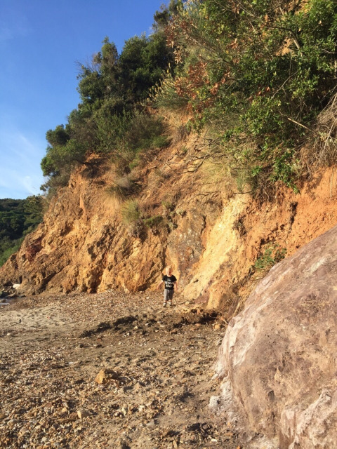 Child walking along a rocky path at the base of a steep hill at Campsite Rosselba le Palme, Tuscany, Italy, in sunlight.