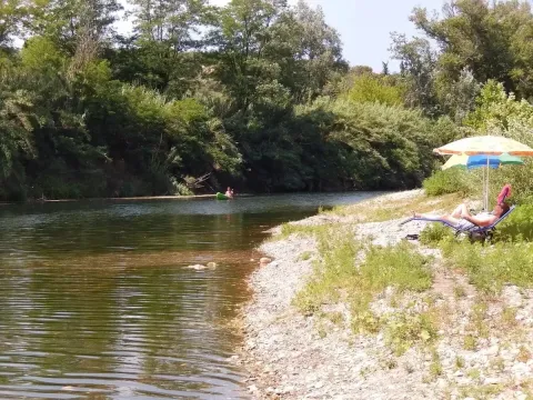 Person slapper af under en paraply ved en flodstrand omgivet af træer på Camping La Plage i Occitanie.
