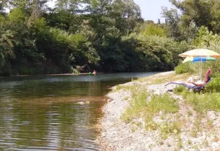 Person slapper af under en paraply ved en flodstrand omgivet af træer på Camping La Plage i Occitanie.