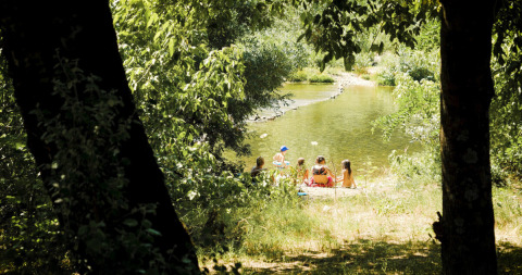 En gruppe mennesker slapper af ved en flod omgivet af træer på Campsite La Plage i Occitanie, Frankrig.