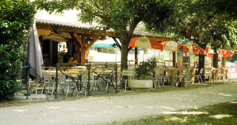 Billedet viser en skyggefuld udendørs café med borde og stole på Campingplads La Plage i Occitanie, Frankrig.