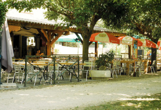 Billedet viser en skyggefuld udendørs café med borde og stole på Campingplads La Plage i Occitanie, Frankrig.