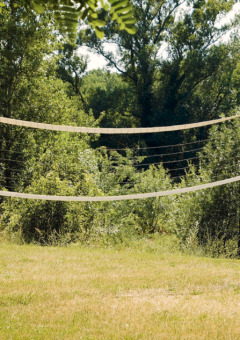 Udendørs volleyballnet med træstolper på en græsplæne omgivet af grønne træer ved Campsite La Plage.