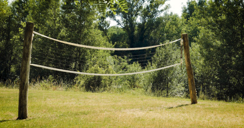 Udendørs volleyballnet med træstolper på en græsplæne omgivet af grønne træer ved Campsite La Plage.