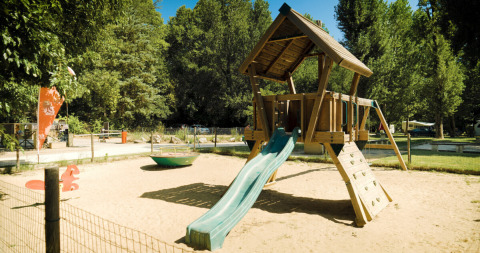 Legeplads i sandet på Campsite La Plage, en feriepark i Occitanie, Frankrig, omgivet af træer og natur.