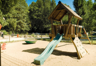 Legeplads i sandet på Campsite La Plage, en feriepark i Occitanie, Frankrig, omgivet af træer og natur.