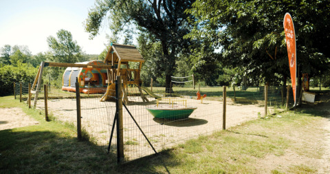 Legeplads med gynger og rutsjebane på campingpladsen La Plage i Occitanie, Frankrig, omgivet af grønne træer.