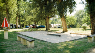 Legeplads og petanquebane i det grønne på Camping La Plage i Occitanie, Frankrig, omgivet af træer.