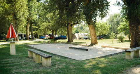 Legeplads og petanquebane i det grønne på Camping La Plage i Occitanie, Frankrig, omgivet af træer.